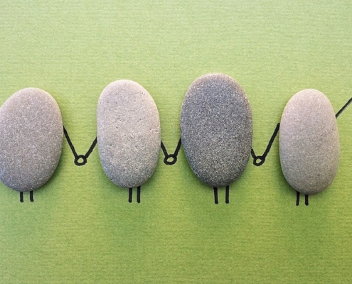 4 flat oval-shaped stones sitting next to each other vertically on a piece of paper with feet and hands holding each other drawn in