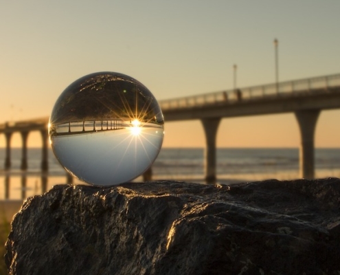 clear glass globe on a rock in front of a pier going out into an ocean, the pier and sky inverted in globe