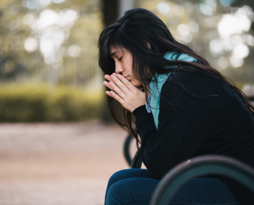 woman wearing a coat and scarf, sitting on a bench praying