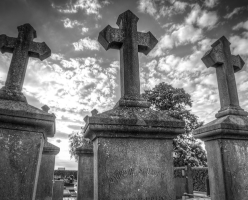 3 old gravestones with crosses on top and sun shining through the clouds in the background