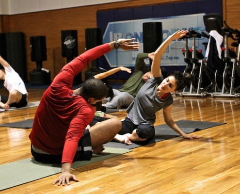 man and woman sitting on yoga mats on a wooden floor, stretching while leaning toward one side