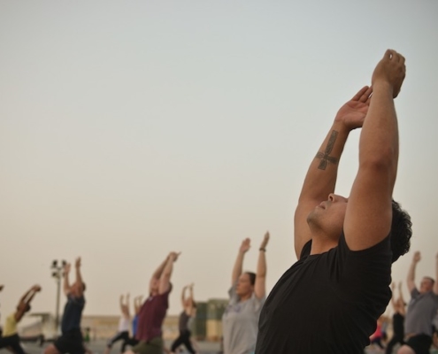 people sitting on beach, stretching their hands in the air while looking upward and focus on one man in foreground