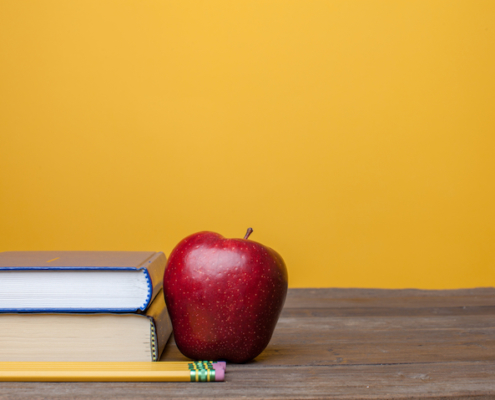 books a red delicious apple and pencil on a plain wooden table with a plain background